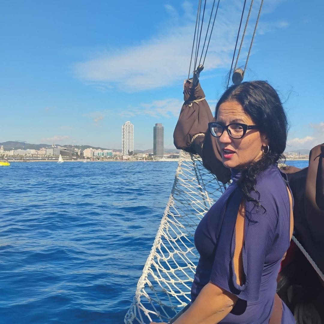 Lole García Ruiz navegando en un velero, con el mar y la costa de Barcelona al fondo